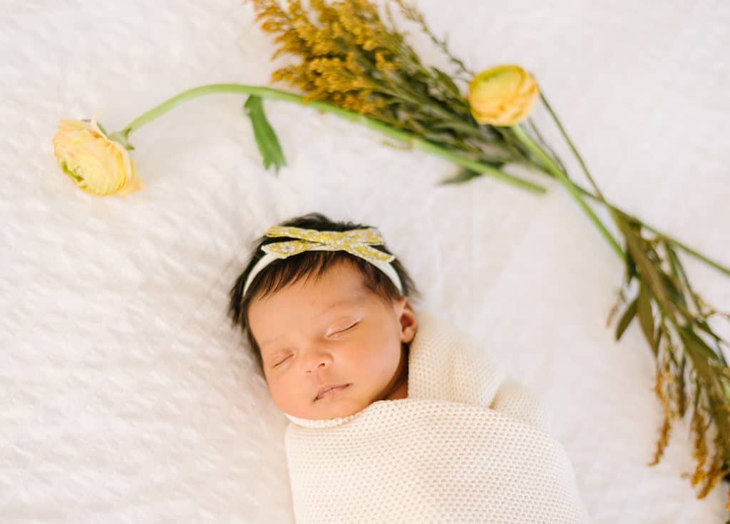 Lifestyle newborn session with fresh flowers white textured backdrop and knit cream swaddle.