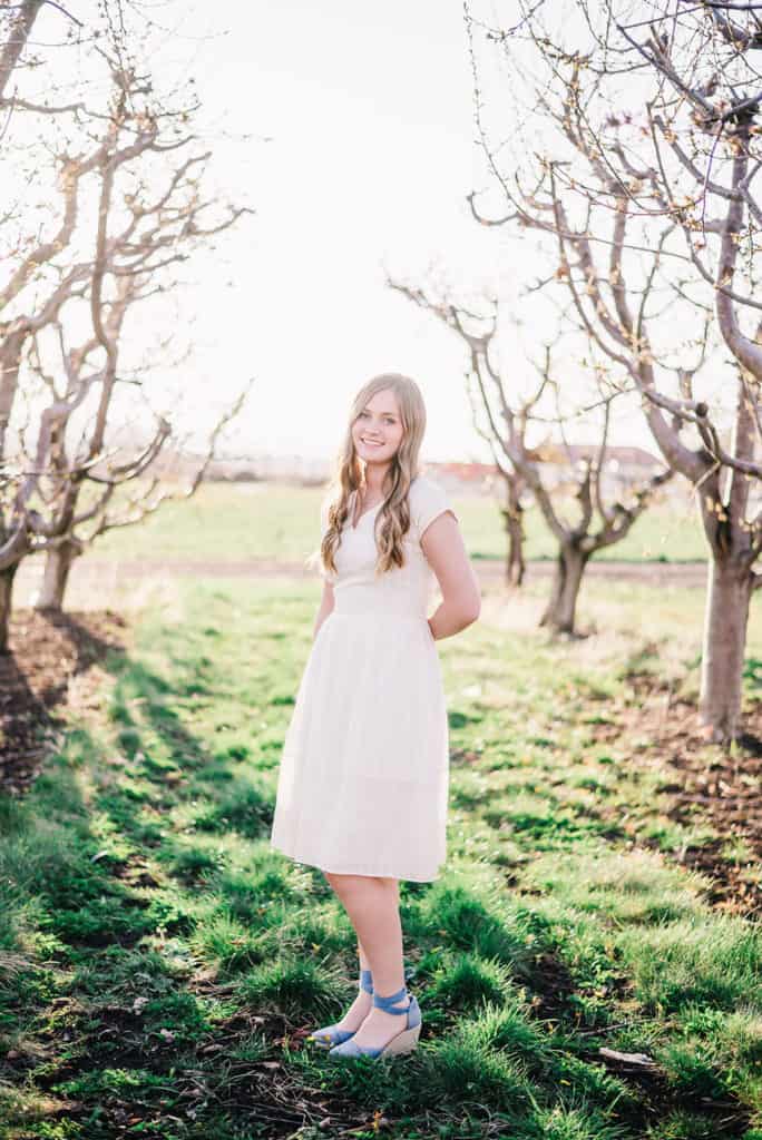 Senior portraits, girl in cream dress poses in front of utah county apple orchard